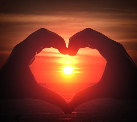 Hand silhouette in heart shape with sunset in the middle