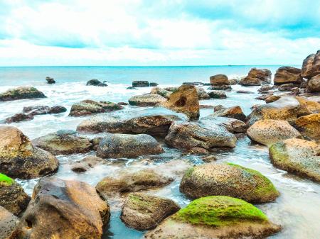 Landscape Photography of Rocks With Moss Surrounded by Body of Water