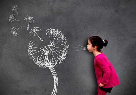Little cute girl blowing dandelion seeds on chalkboard