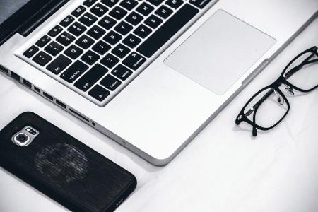 Macbook Beside Eyeglasses and Smartphone