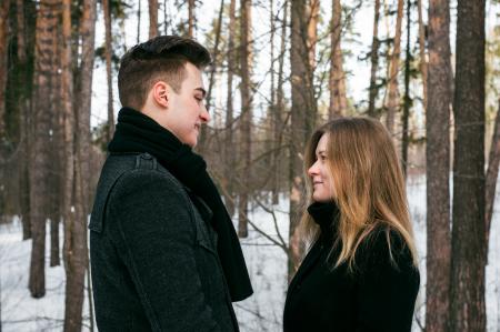 Man and Woman Wearing Black Coats Standing Near Snow-covered Trees