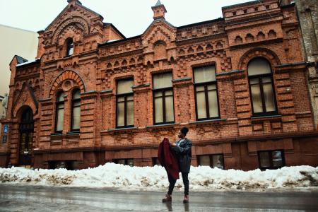 Man Holding Red Coat Standing on Street Near Brown Building