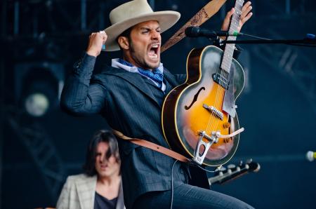 Man in Black Formal Suit Holding Electric Guitar While Raising His Right Hand and Opening His Mouth in Tilt Shift Lens Photography