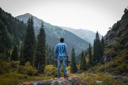 Man in Blue and White Checked Quarter-sleeved Shirt Holding Black Camera Standing on Rock