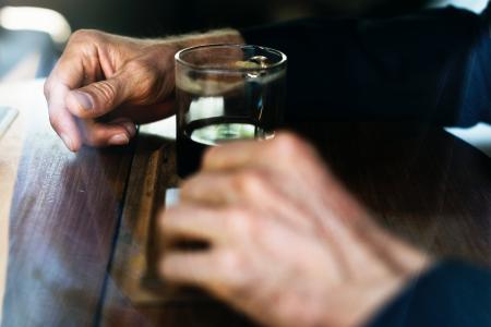 Man in Blue Long Sleeve Shirt In Front Of Drinking Glass On Brown Wooden Table