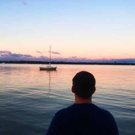 Man in Blue Shirt Near Blue Sea and White Boat Under Blue Sky