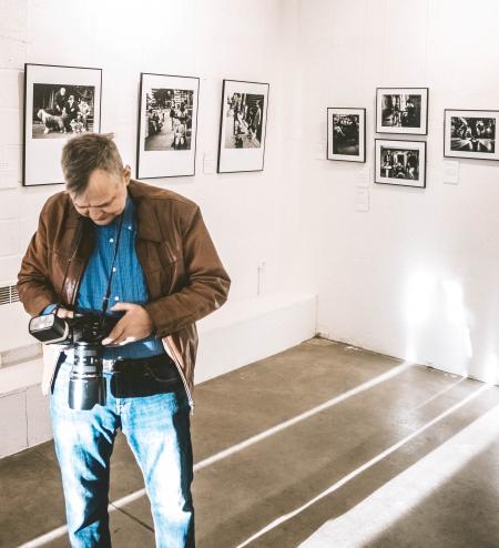 Man in Brown Jacket, Blue Denim Jeans and Blue Dress Shirt Holding Dslr Camera