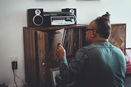 Man in Gray Longsleeve Shirt Holding Book in Front of Brown Wooden Book Case