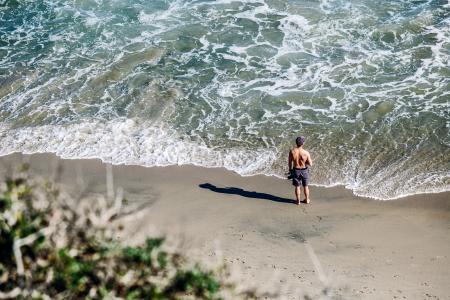 Man in Gray Shorts Standing on White Sand Beach during Daytime