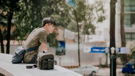 Man in Green and Beige Camouflage T-shirt Siting Beside Bag at Daytime