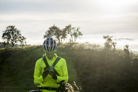 Man in Green Bicycle Suit Standing While Using His Smartphone