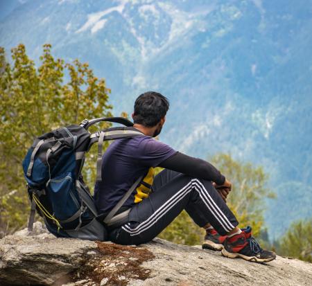 Man in Purple T-shirt With Blue Backpack Sitting on Gray Boulder