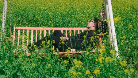 Man in White and Brown Canopy Swing Surrounded With Yellow Petal Flower