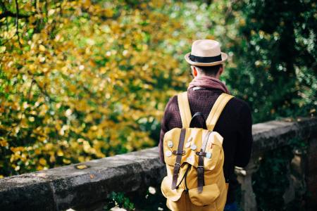 Man in White Fedora Hat and Beige Knapsack Beside Grey Concrete Railings during Daytime