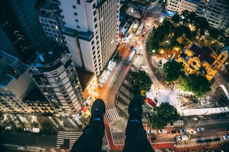 Man Sitting on High Rise Building Taking Photo Below