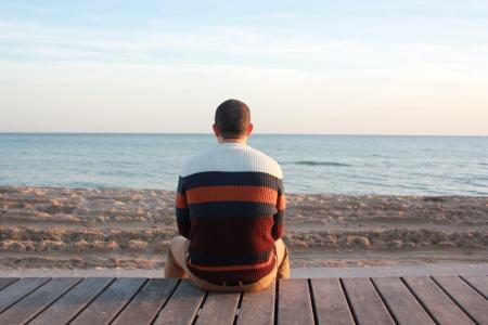 Man Sitting on Wooden Panel Facing in the Ocean