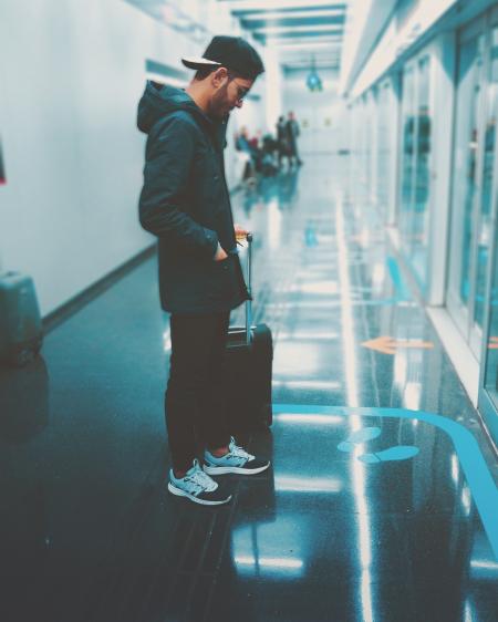 Man Stands Front of Glass Panel While Holding Luggage