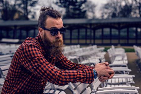 Man Wearing Black and Red Checkered Long Sleeve Shirt Wearing Black Wayfarer Sunglasses Sitting on White Wooden Chair