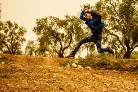 Man Wearing Blue and Black Shirt Jumping While Holding Brown Jacket Taken during Golden Hour