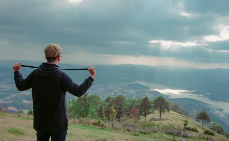 Man Wearing Hoodie Standing on Mountain Under Cloudy Sky