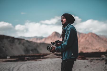 Man Wearing Jacket Holding Dslr Camera on Desert