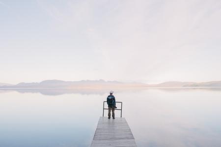 Man Wearing Jacket Standing on Wooden Docks Leading to Body of Water