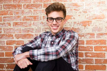 Man Wearing Plaid Dress Shirt And Black Pants Sitting Near Brown Brick Wall