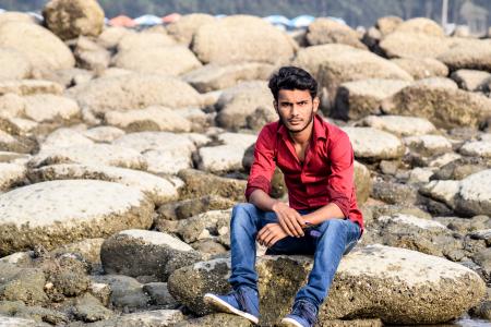 Man Wearing Red Dress Shirt and Blue Jeans White Sitting on Gray Stone Formation