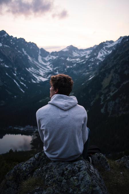 Man Wearing White Hoodie Sitting on a Rock With a View on Mountain