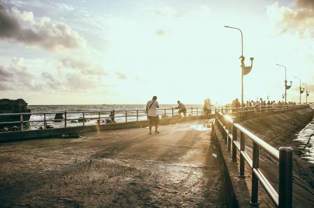 Man Wearing White Shirt Walking on Concrete Pavement Near Sea