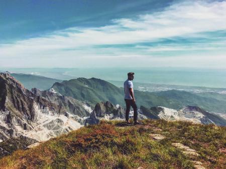 Man Wearing White T-shirt Standing on Mountain Under Blue Cloudy Sky