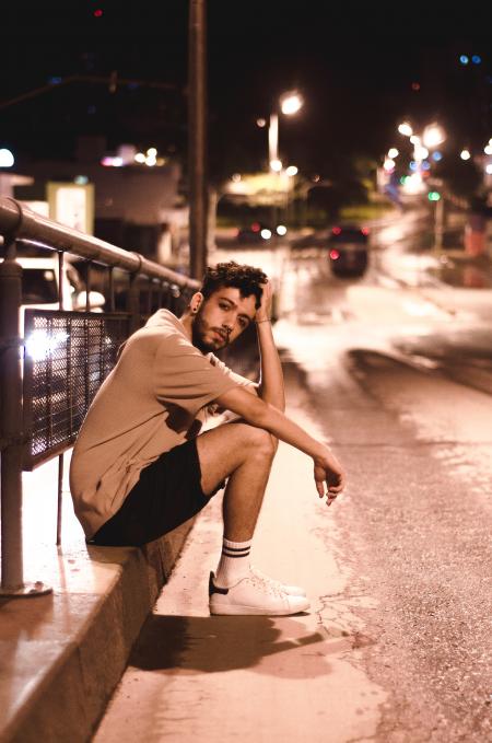 Man Wears Brown Shirt and Black Shorts Seats Beside Black Street Post