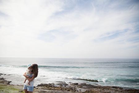 Mother Holding Her Baby in Front of Seashore during Daytime