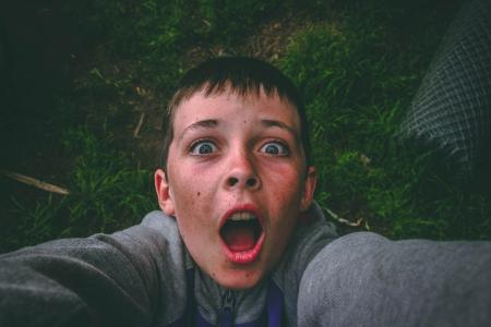 Opened Mouth Black Haired Boy in Gray Full-zip Jacket Standing on Grass Field Taking Selfie