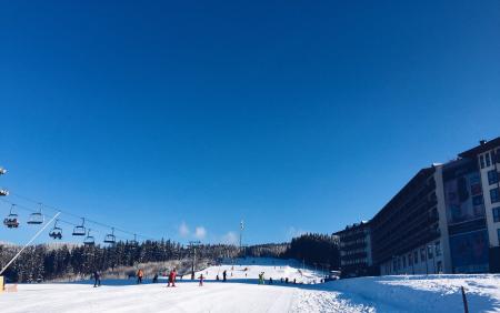 People on a Snowy Ski Hill With a Lift on the Left and a Hotel on the Right