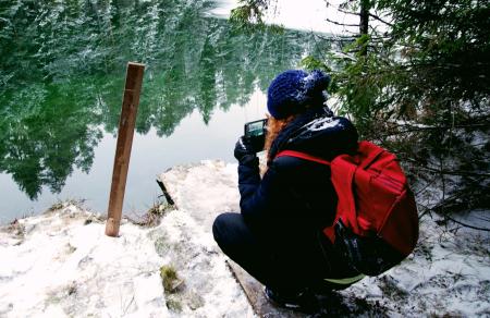 Person Carrying Red Backpack Capturing Photo Of Body Of Water