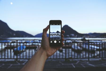 Person Holding Iphone Taking Picture of Mountain Near Body of Water