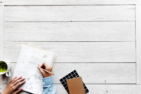 Person Holding Pencil While Writing on White Paper