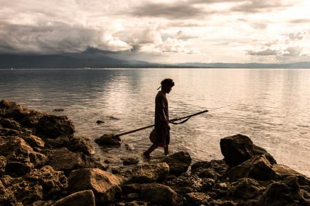 Person Holding Spear Beside Body of Water