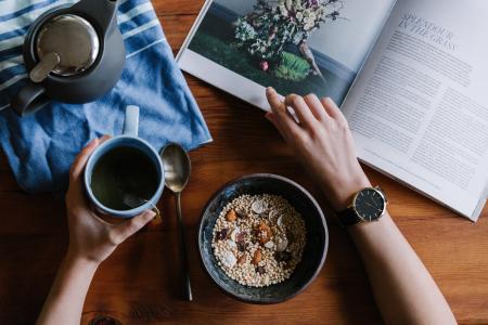 Person Holding White Ceramic Coffee Cup Leaning on Brown Wooden Table