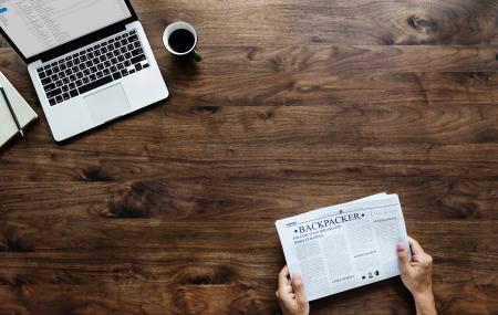 Person Holding White Newspaper on Brown Wooden Surface