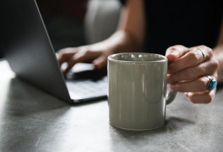 Person in Black Top Holding White Ceramic Mug and Using Laptop Computer