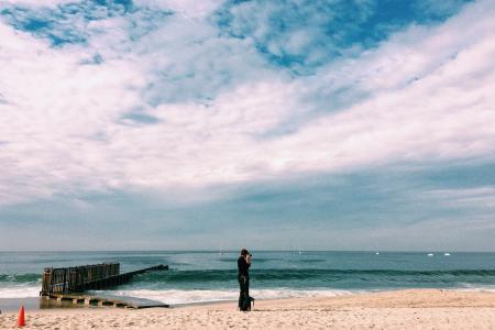 Person in Black Top Standing on Seashore Under White Clouds