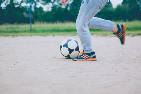 Person Kicking Soccer Ball on Gray Sand