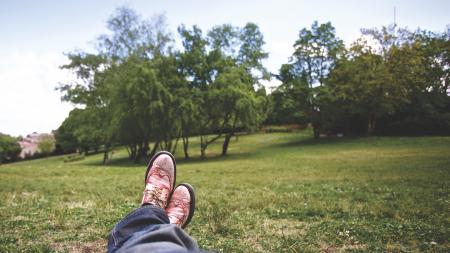 Person Lying on Grass Field Near Trees Under White Clouds during Daytime