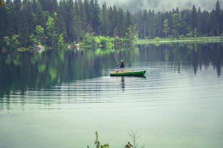 Person on Green Boat Fishing on Body of Water