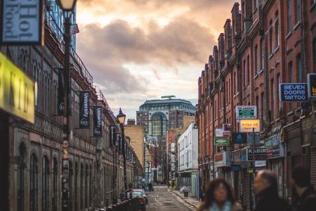 Person on Road Between Brown Walled Building during Daytime Under Cumulus Clouds