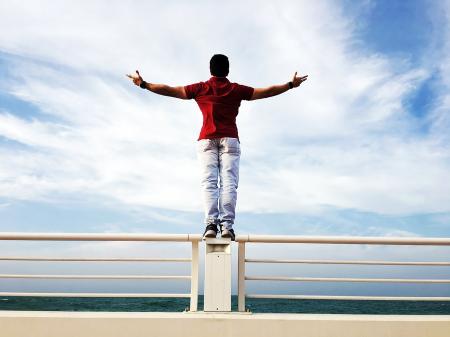 Person Raising Hands Mid-air Sidewards While Standing on Gray Steel Railings