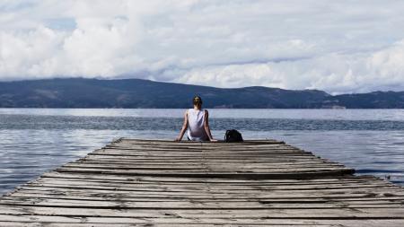 Person Sitting on Brown Wooden Dock Under Cloudy Blue Sky