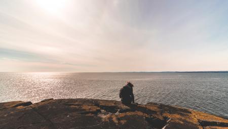 Person Sitting on Stone in Front of Sea Water